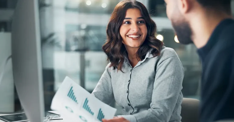 Smiling businesswoman reviews contract performance charts with a colleague, representing collaboration and KPI tracking in contract management.