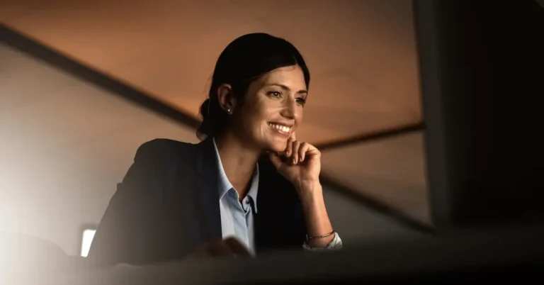 Professional woman smiling and working at a computer in a modern office, representing efficiency with contract redlining software.