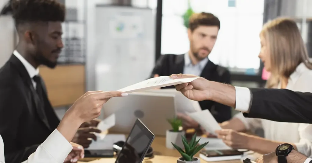 Business professionals in a meeting exchanging documents, symbolizing procurement strategies and contract management for mitigating tariff impacts.