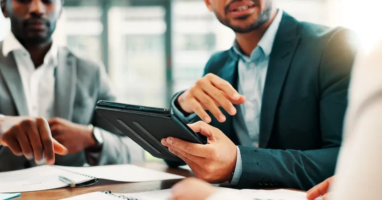 Business professionals in a meeting reviewing documents and a tablet, symbolizing collaboration and strategy in contract compliance initiatives.