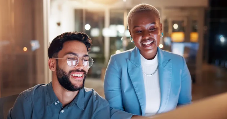 Two professionals smiling while reviewing data on a computer screen, representing collaboration and efficiency enabled by AI contract data extraction.