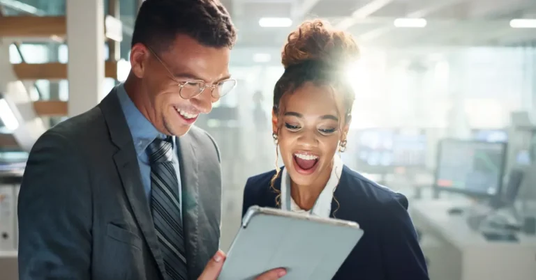 Two business professionals in formal attire smile while reviewing information on a tablet in a bright, modern office, symbolizing innovation and collaboration in AI-powered legal and compliance operations.