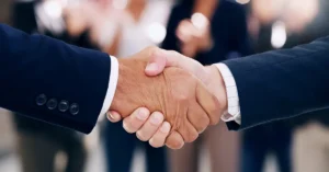 Two business professionals in suits shaking hands, symbolizing the Proxiio and ContractPodAi partnership to deliver scalable contract intelligence solutions.