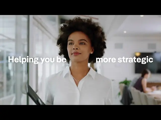 Confident woman in a white blouse holding a laptop walks through a bright modern office, overlaid text reads “Helping you be more strategic.”