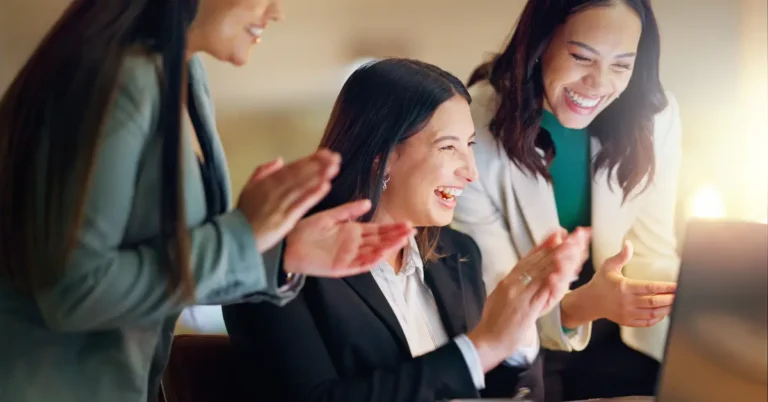 Business professionals smiling and clapping while gathered around a laptop, celebrating their Gold Stevie® Award win.