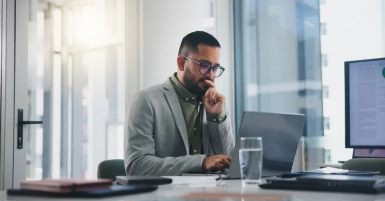 Professional man in glasses and suit jacket working thoughtfully on a laptop in a bright office, symbolizing secure digital contract management.