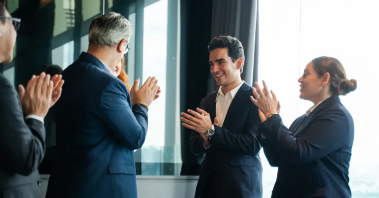 Business professionals in formal attire applaud a smiling colleague in a modern office, celebrating a leadership team announcement at ContractPodAi.