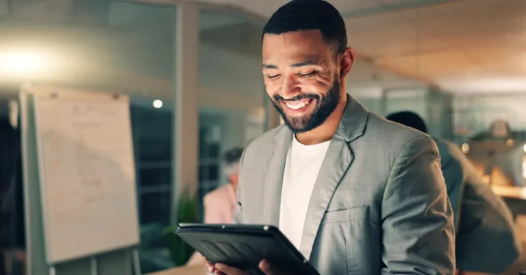 Smiling business professional in a modern office reviews contract lifecycle management (CLM) strategies on a digital tablet during an evening meeting.